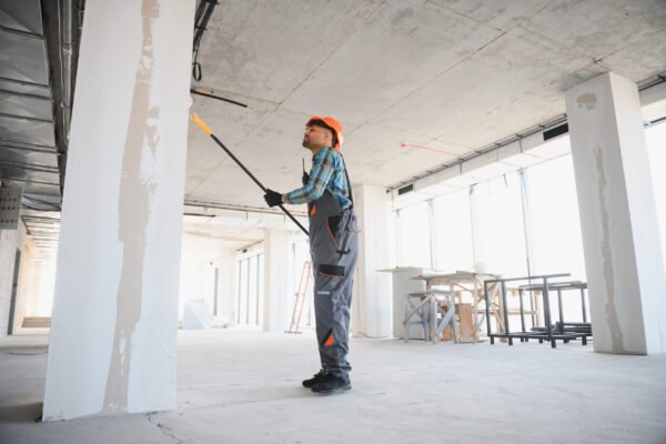Construction worker applying a coat of paint on a wall using a roller, working diligently on a building site