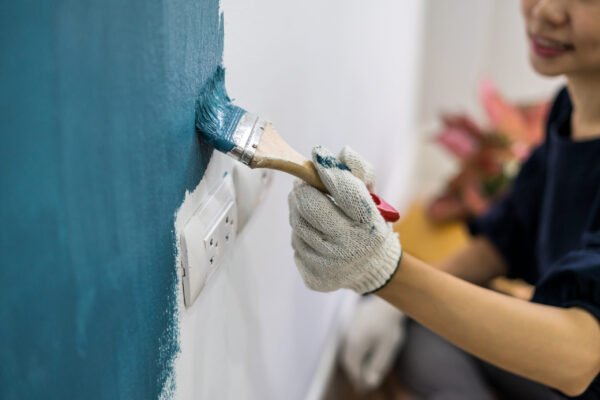 Young asian happy woman painting interior wall with paint brush in new house