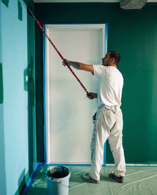 Professional painter using a telescopic paint roller painting a wall green in a house during renovation works
